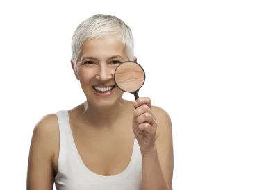 White middle-aged woman with short white hair holding a magnifying glass to her cheek.