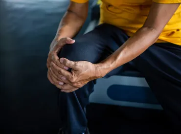 Senior Asian man in work-out gear holding an aching knee.