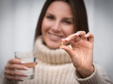 Woman holding a fish oil capsule in one hand and a glass of water in the other.