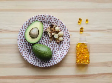 Plate with a halved avocado on it, nuts, and fish oil supplements to the side of plate.