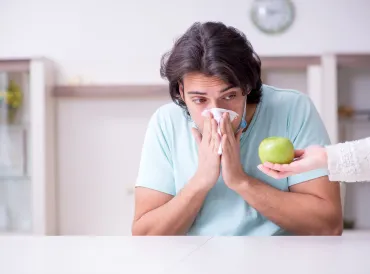 Young man looking at fruit and sneezing into a tissue.