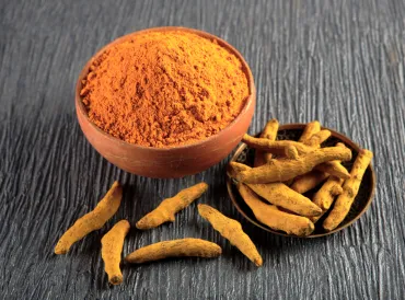 A bowl of orange turmeric with ginger around it.