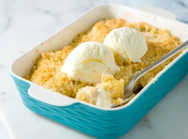 Aqua baking pan filled with fruit crumble with two small scoops of ice cream on top.