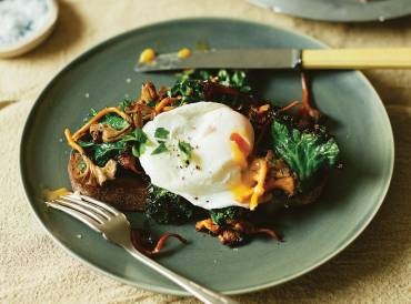 Chanterelle Toast with Poached Eggs and Kale on a plate with yolk pouring out of the egg.