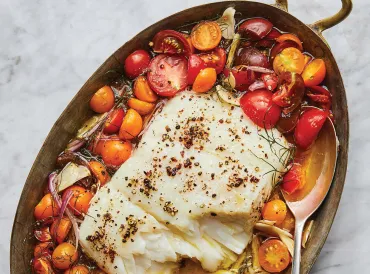 pan of roasted tomatoes topped by fillet of fish