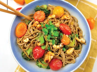a bowl of noodles with cherry tomatoes and candied cashews
