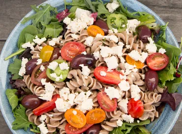 A bowl of pasta salad topped with vegan tofu feta