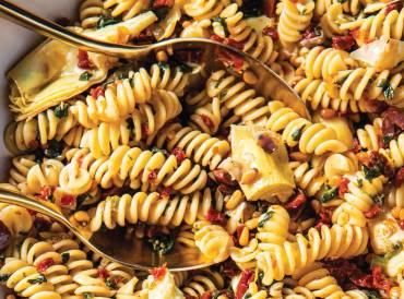 a bowl of fusilli with spinach, artichokes, and sun-dried tomatoes