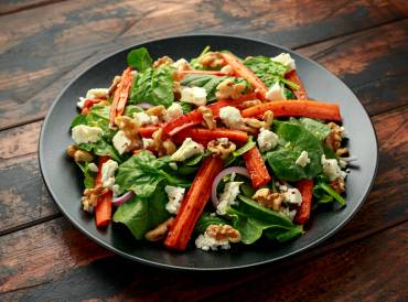 Grey salad plate filled with spinach, roasted carrots, cheese, and walnuts.