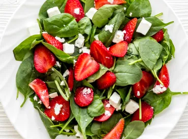 a plate of spinach, crumbled feta, and sliced strawberries
