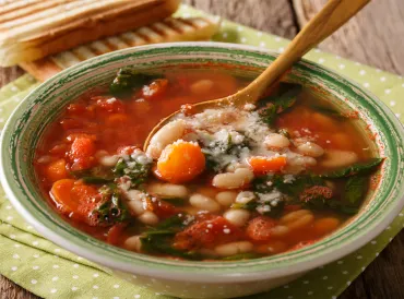 a bowl of tomato-based soup with beans and spinach