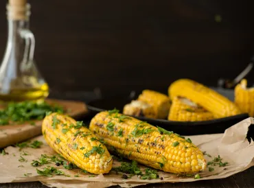 Grilled Lime & Cilantro Corn on the Cob on parchment paper with corn, oil and cilantro in the background.