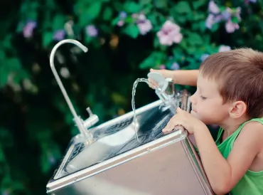 a young boy drinking from a water bubbler fountain in the park