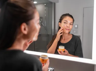 A woman adding honey to her skin in front of a bathroom mirror. 