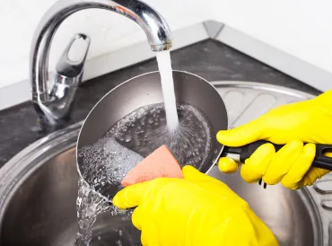 scrubbing a frying pan under hot water
