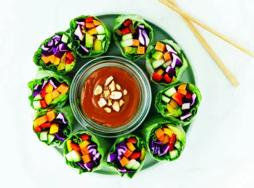 Colorful veggies wrapped in lettuce, positioned vertically around a dish of hoisin sauce.
