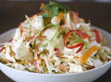 White bowl of green cabbage and bell pepper cole slaw.