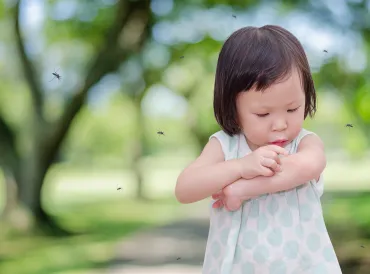 A little girl being swarmed by mosquitos, scratching a bite.