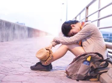 An exhausted woman sitting against a railing with her head on her knees