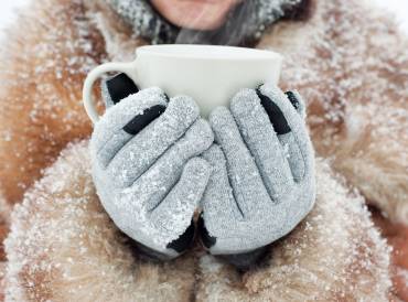 a young woman holding a steaming mug with winter gloves