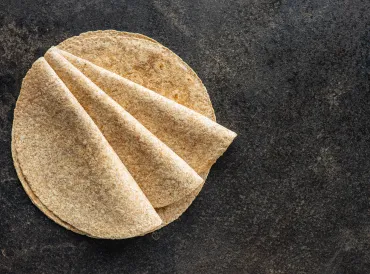 Several whole-grain tortillas folded on a gray granite surface.