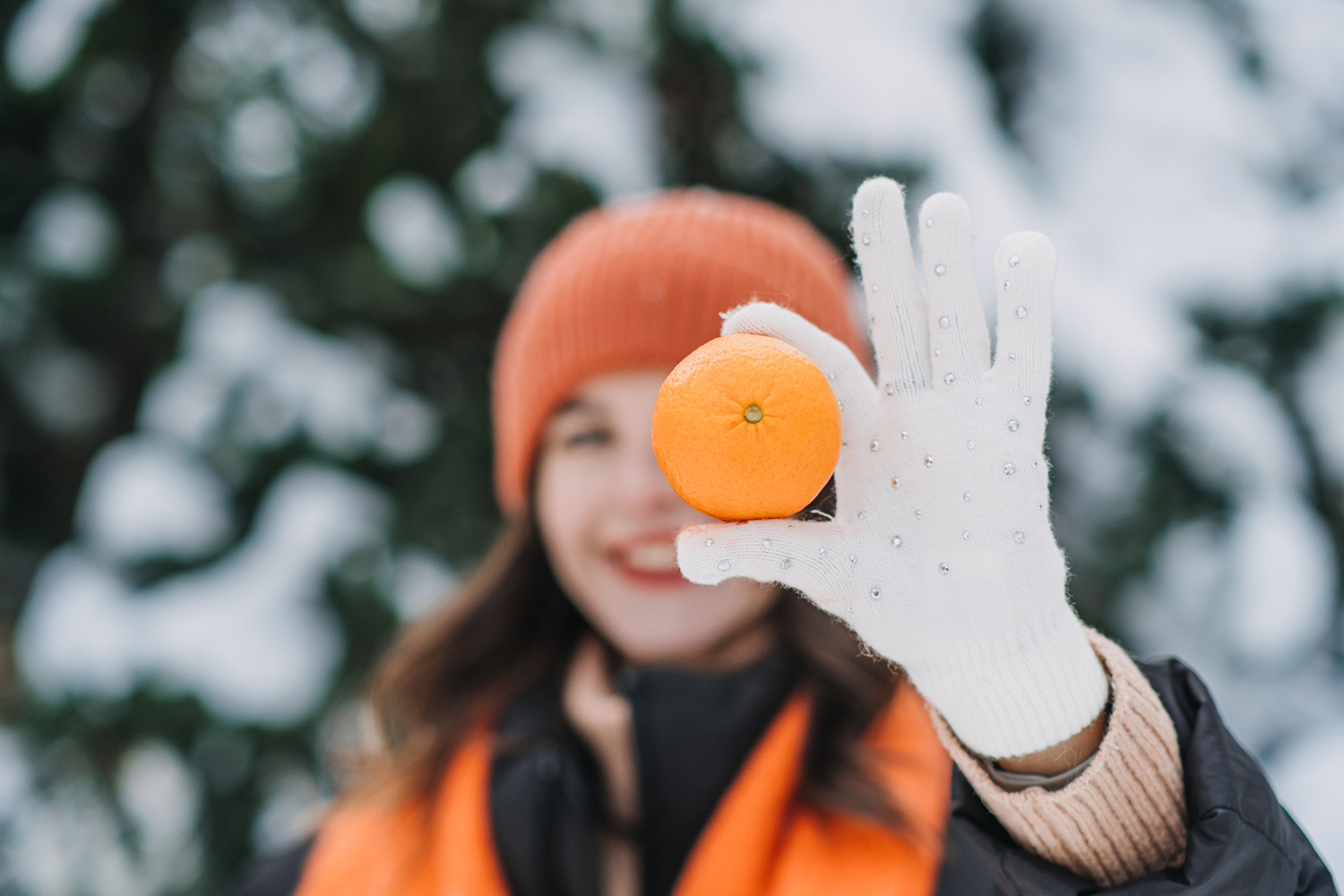 a healthy woman outdoors in winter holding up an orange