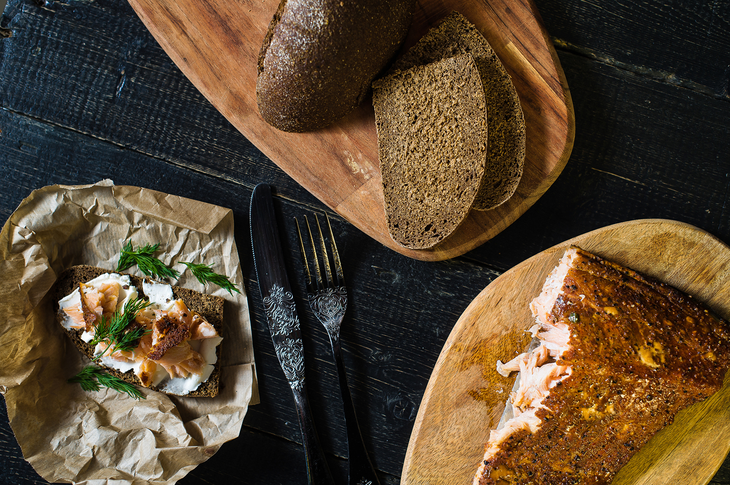 Scandinavian sandwich with smoked salmon fillet on black bread with soft cheese on a black wooden table.