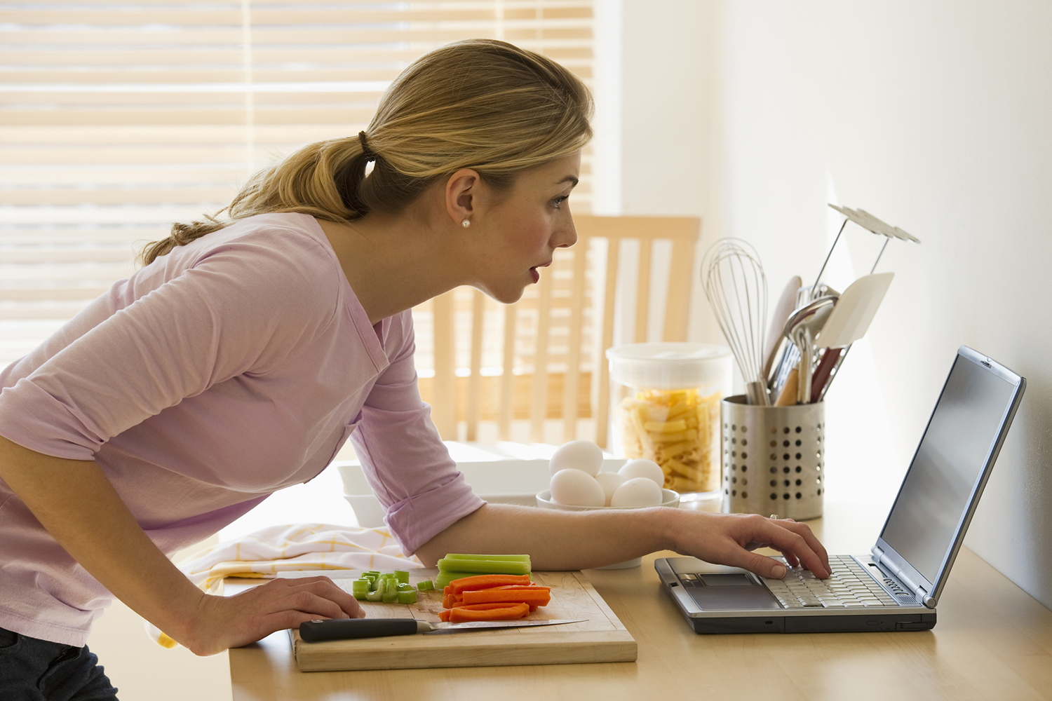 a woman in the kitchen checking her laptop for tips and tricks
