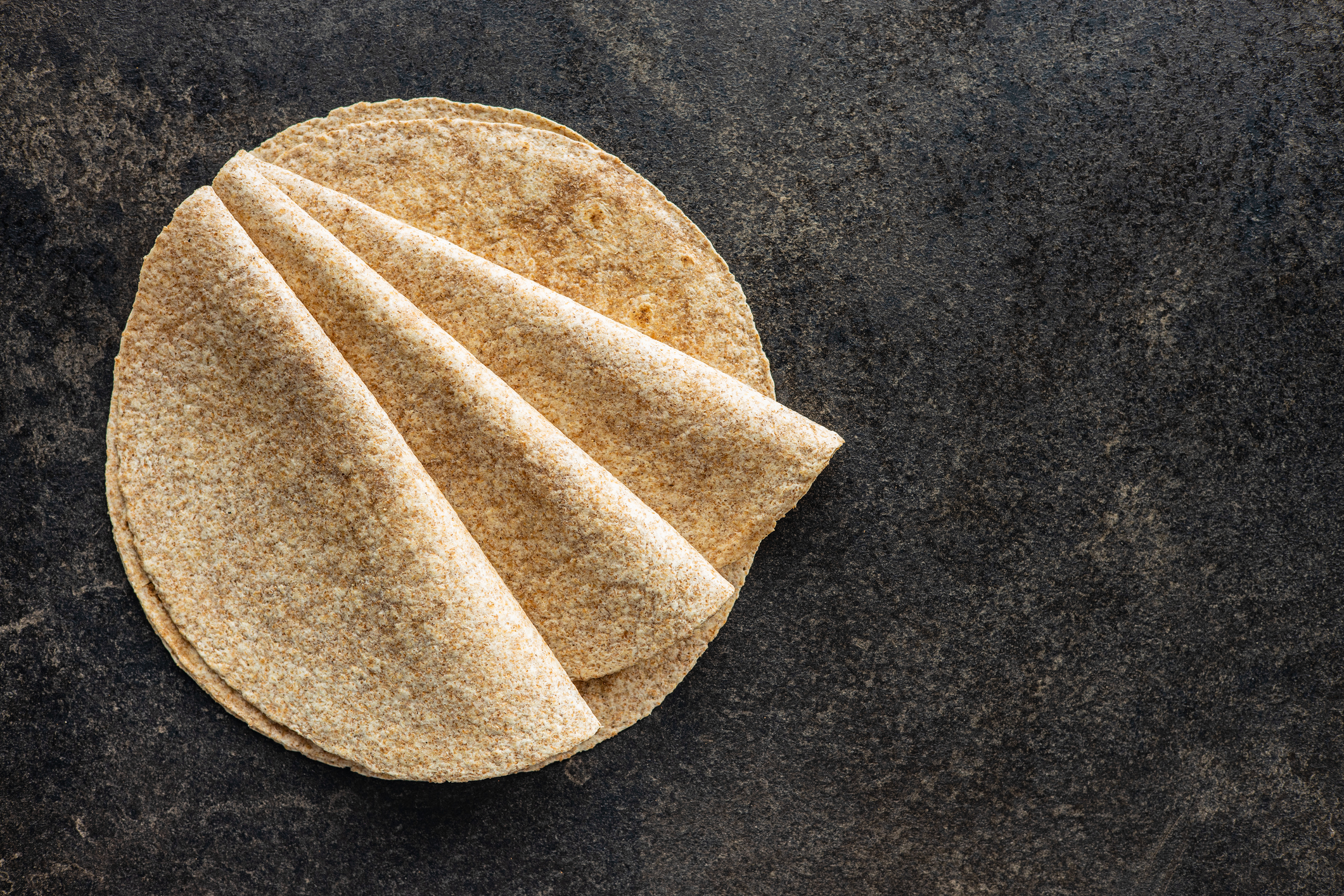 Several whole-grain tortillas folded on a gray granite surface.